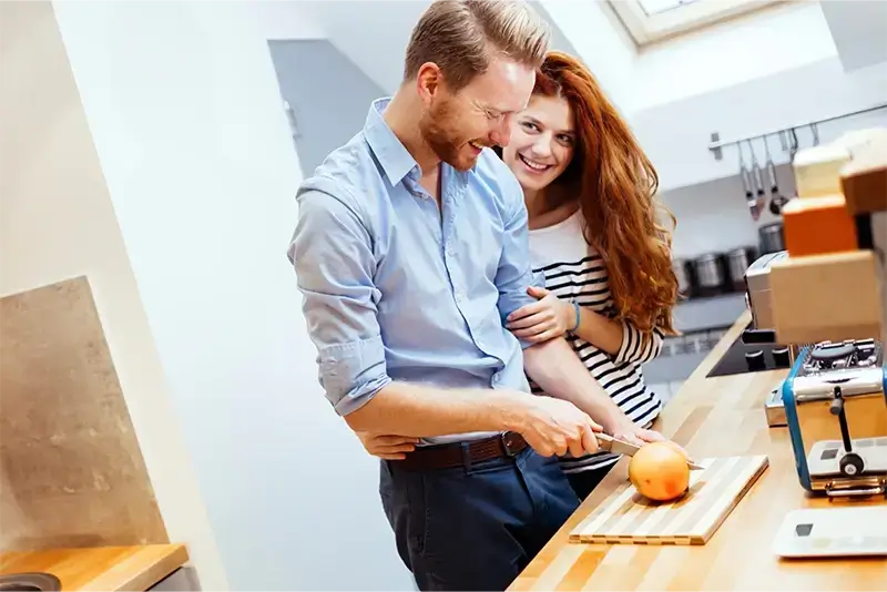 Ein junges Paar steht nach einer Umschuldung fröhlich in der Küche seiner Wohnung.