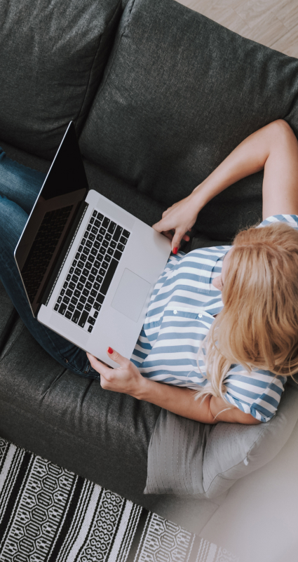 Auf dem Sofa sitzende Frau schaut auf ihren Laptop-Bildschirm